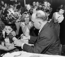 Patsy Murr, first grader at Fulton School in Lancaster, Pa., gets her Salk shot from Dr. Norman E. Snyder as she is held by Mrs. Walter Sourweine, April 25, 1955. Others view the proceedings with mixed emotions